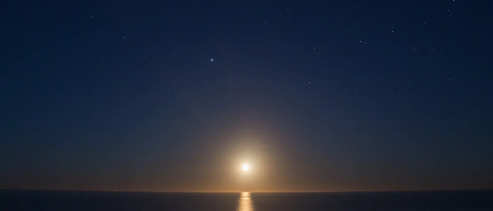 La luna sobre un mar en calma, con su reflejo trazando una línea de luz