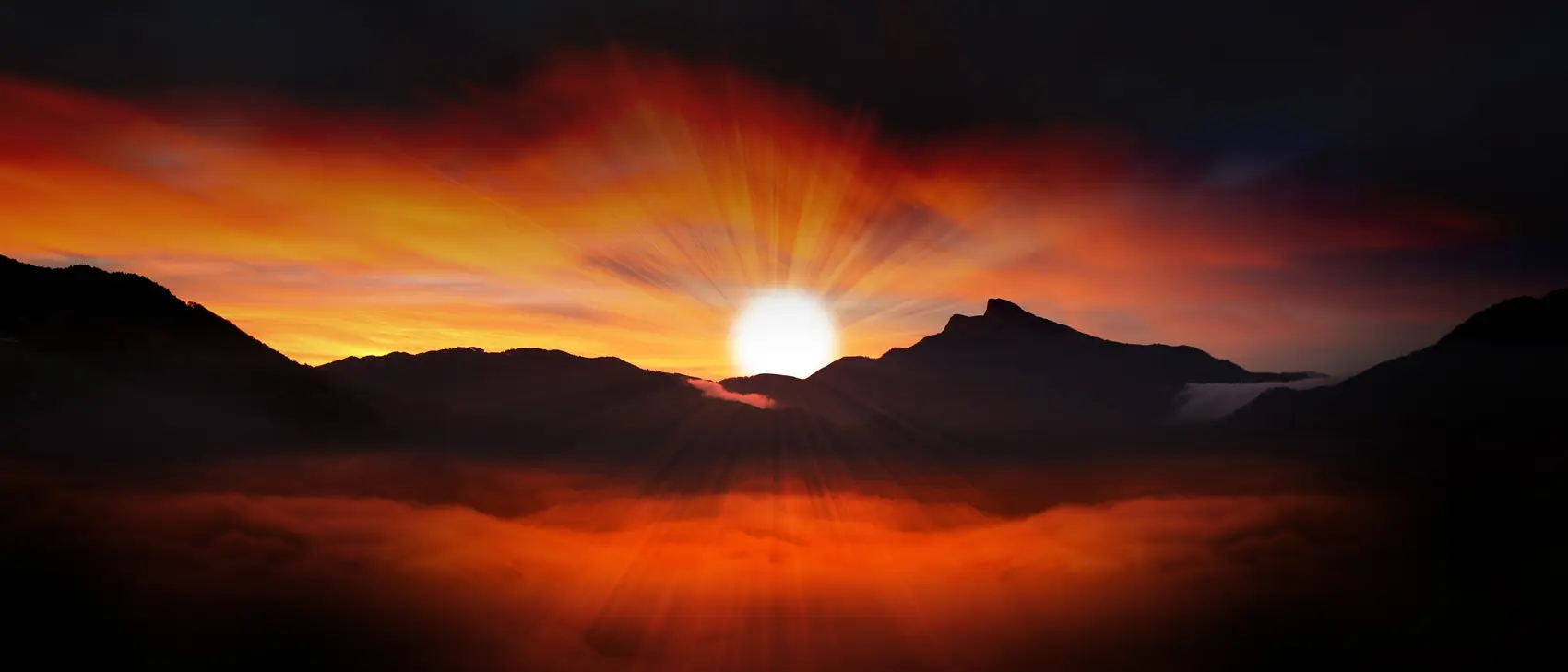 Amanecer rompiendo sobre unas montañas oscuras, con niebla en el valle